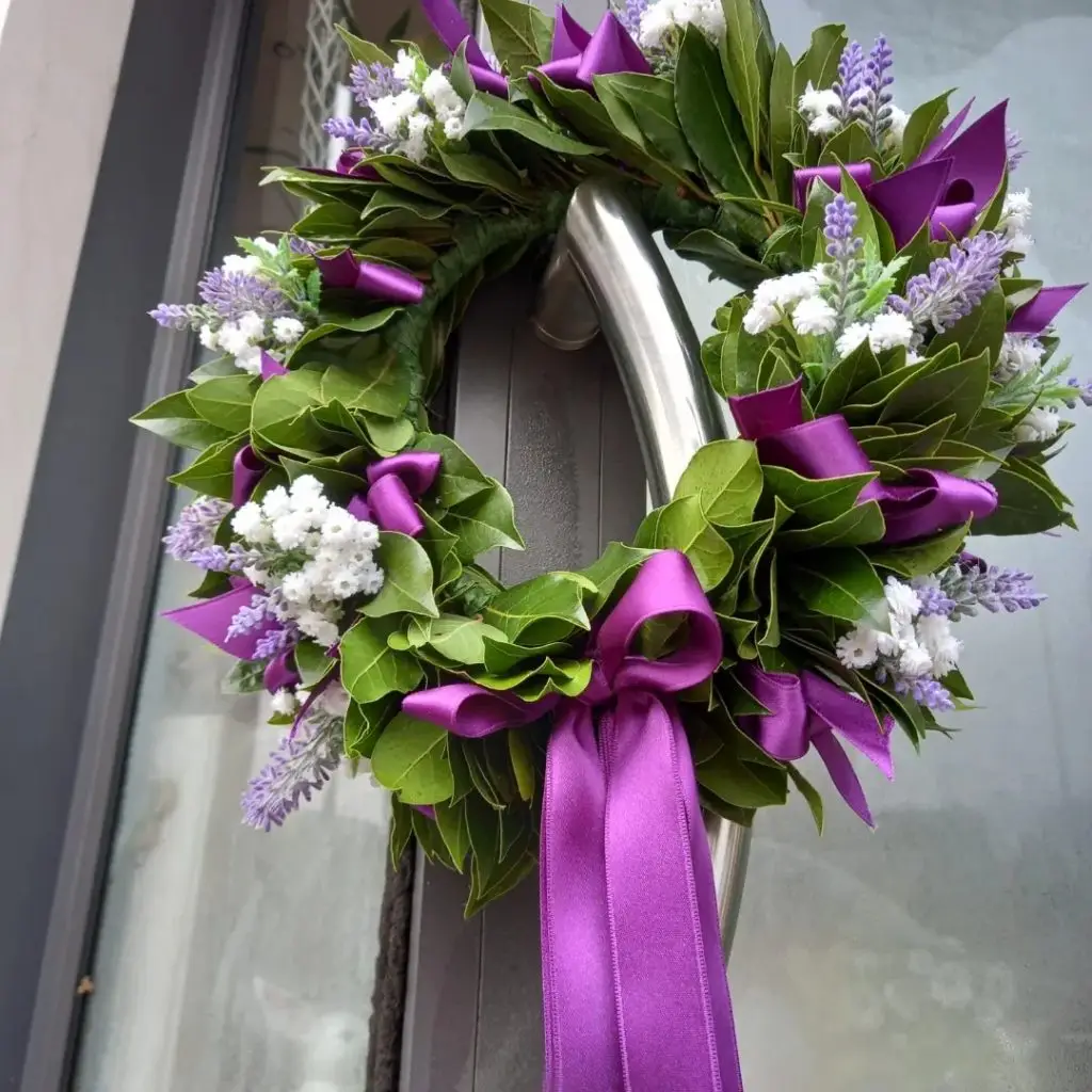 corona d'alloro con nastro lilla e fiori bianchi